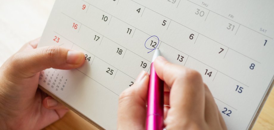 calendar page with female hand holding pen on desk table