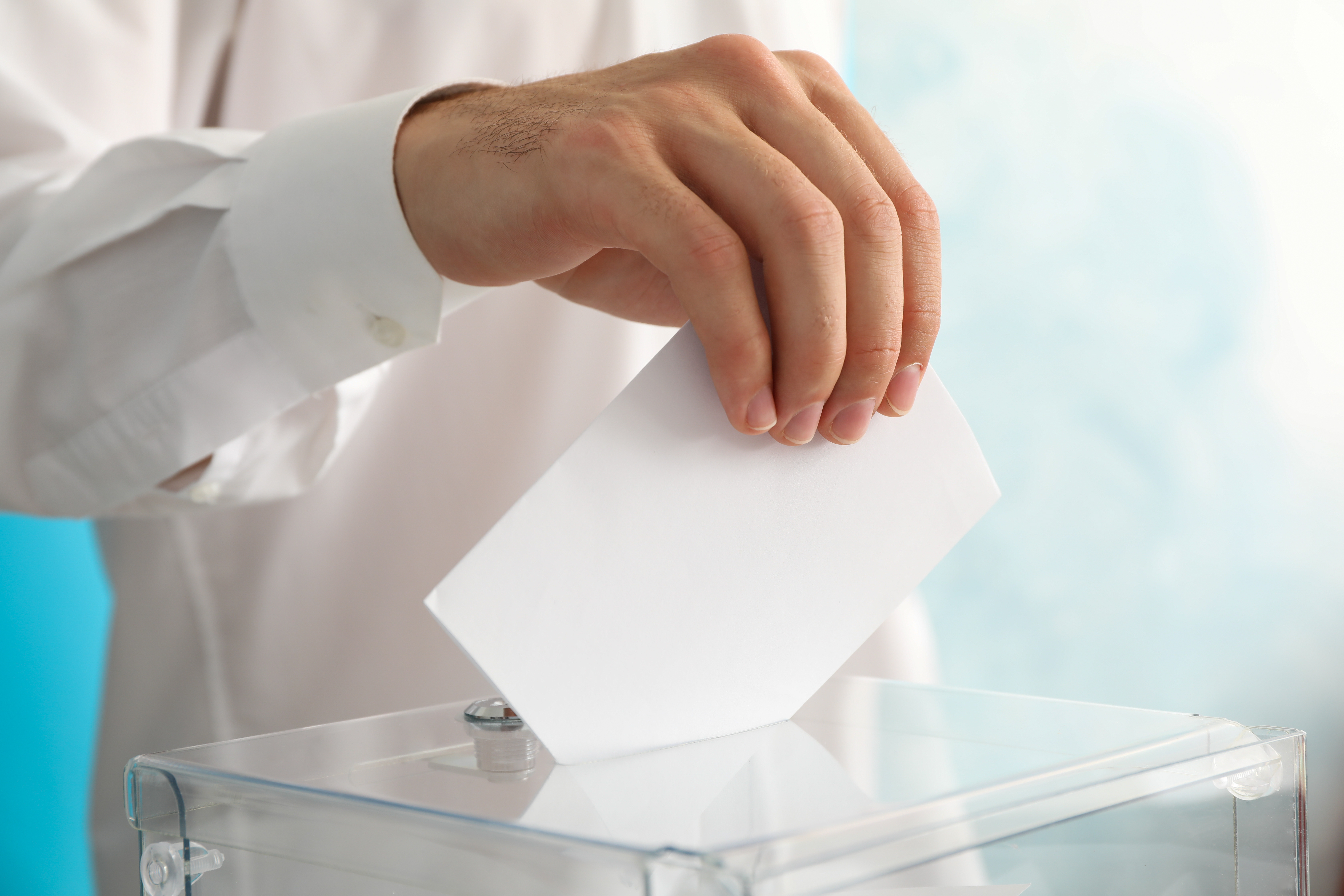 Man putting ballot into voting box against blue background