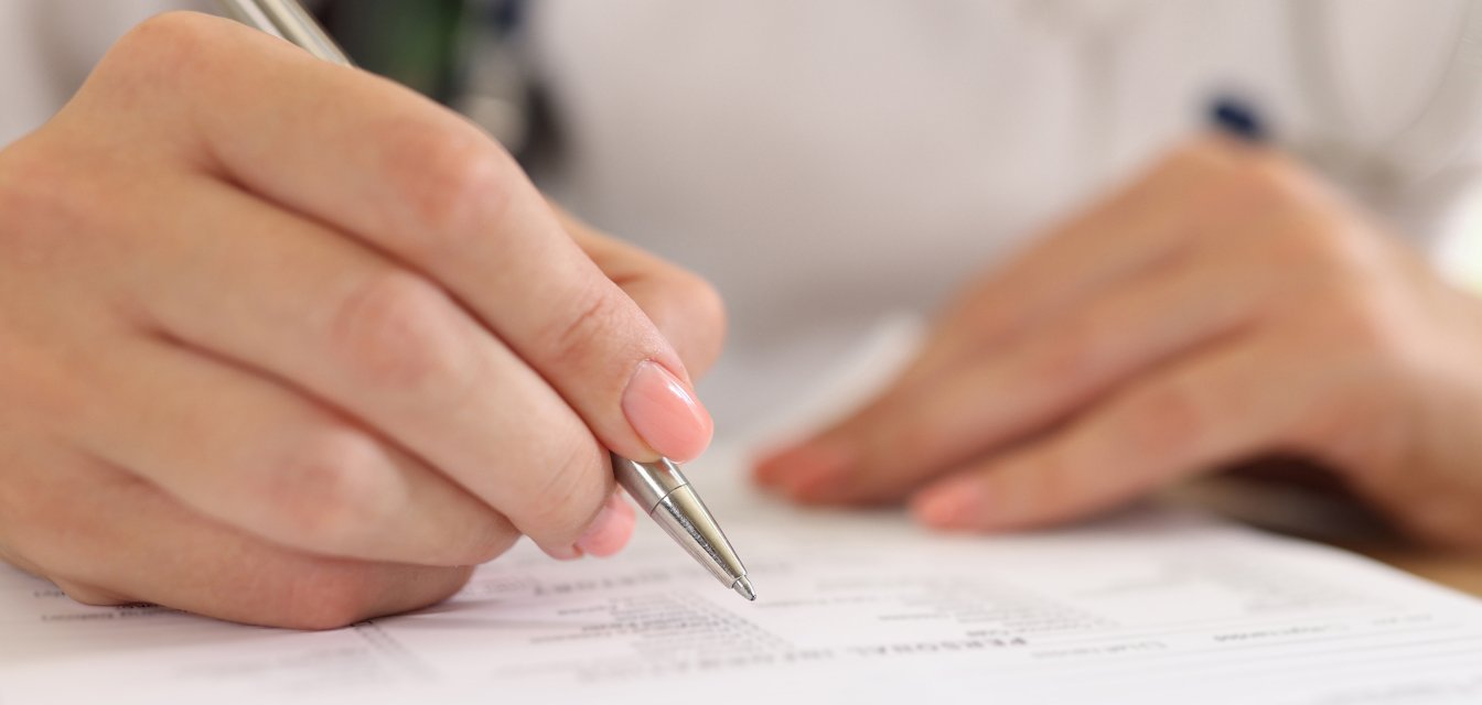 Female doctor fills out medical forms while sitting at her desk in clinic.